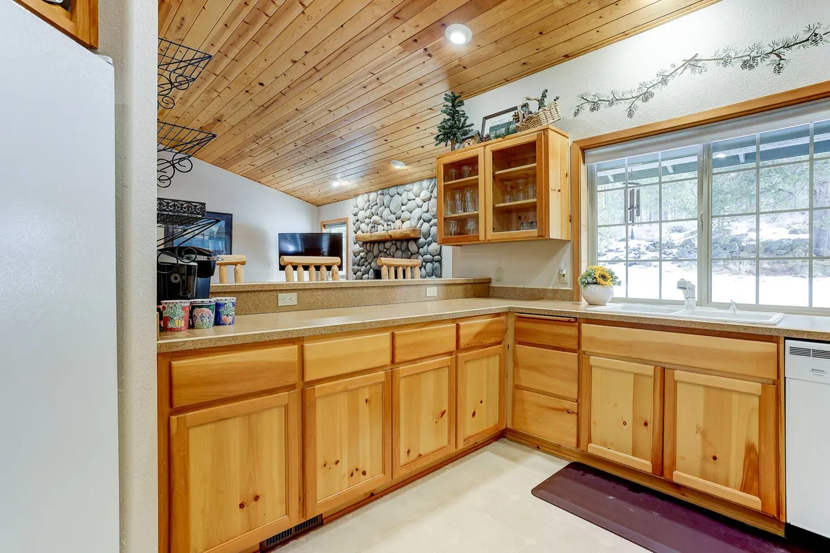 A cozy interior with a stone fireplace, wooden cabinets, and a large window bringing in natural light. The space is inviting, ideal for gathering after a day of adventure to relax, share stories, and unwind.