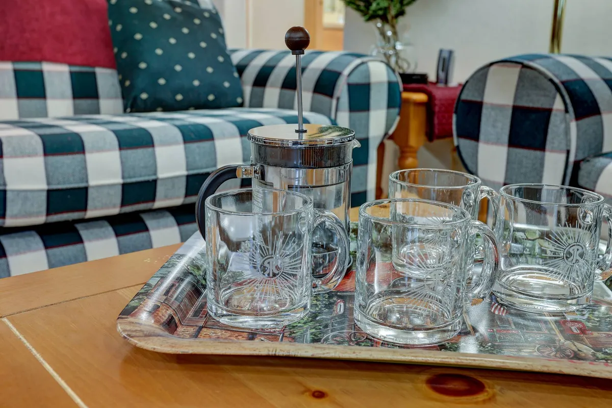 A close-up view of a plaid sofa with a French press and glass mugs on the coffee table, set in a cozy nook ideal for intimate conversations or sharing a warm drink after a day's adventure.