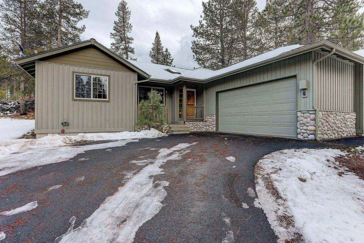 This image features the front entrance of the home with a welcoming porch, visible garage door, and stonework along the base. The surrounding area offers hints of open yard, ideal for seasonal outdoor activities and gatherings.