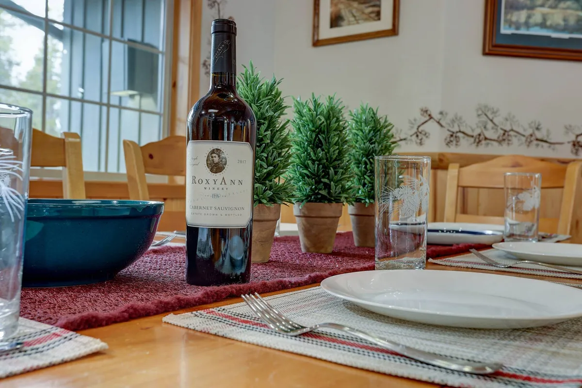 A warmly lit dining area featuring a beautifully set table with a wine bottle, green plants, and comfortable dining chairs, ideal for group gatherings and sharing meals after a day of outdoor adventures.