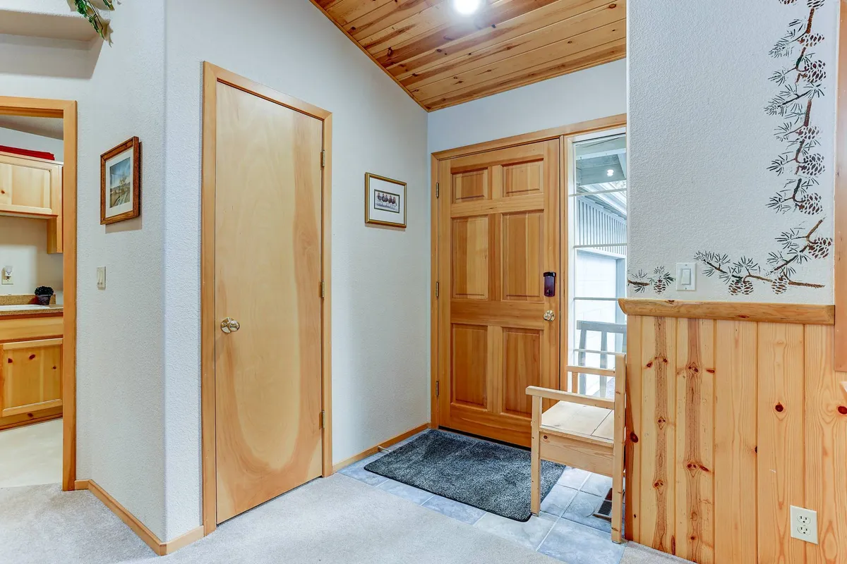 A welcoming front entryway featuring a wood-accented door, decorative wall art, and a wooden bench, suggesting a warm first impression and a connection to the tranquil, mature neighborhood setting. The scene hints at arriving home after a day of exploring Sunriver or enjoying its resort amenities.