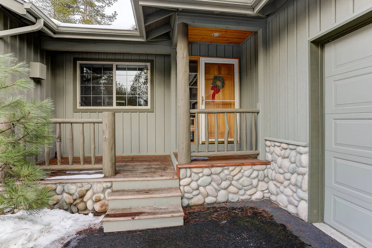 The image shows a welcoming front door decorated with a wreath, stone steps leading up to the entrance, and a wooden railing. The scene is warm and inviting, hinting at the transition between private home life and the vibrant world just beyond the door.