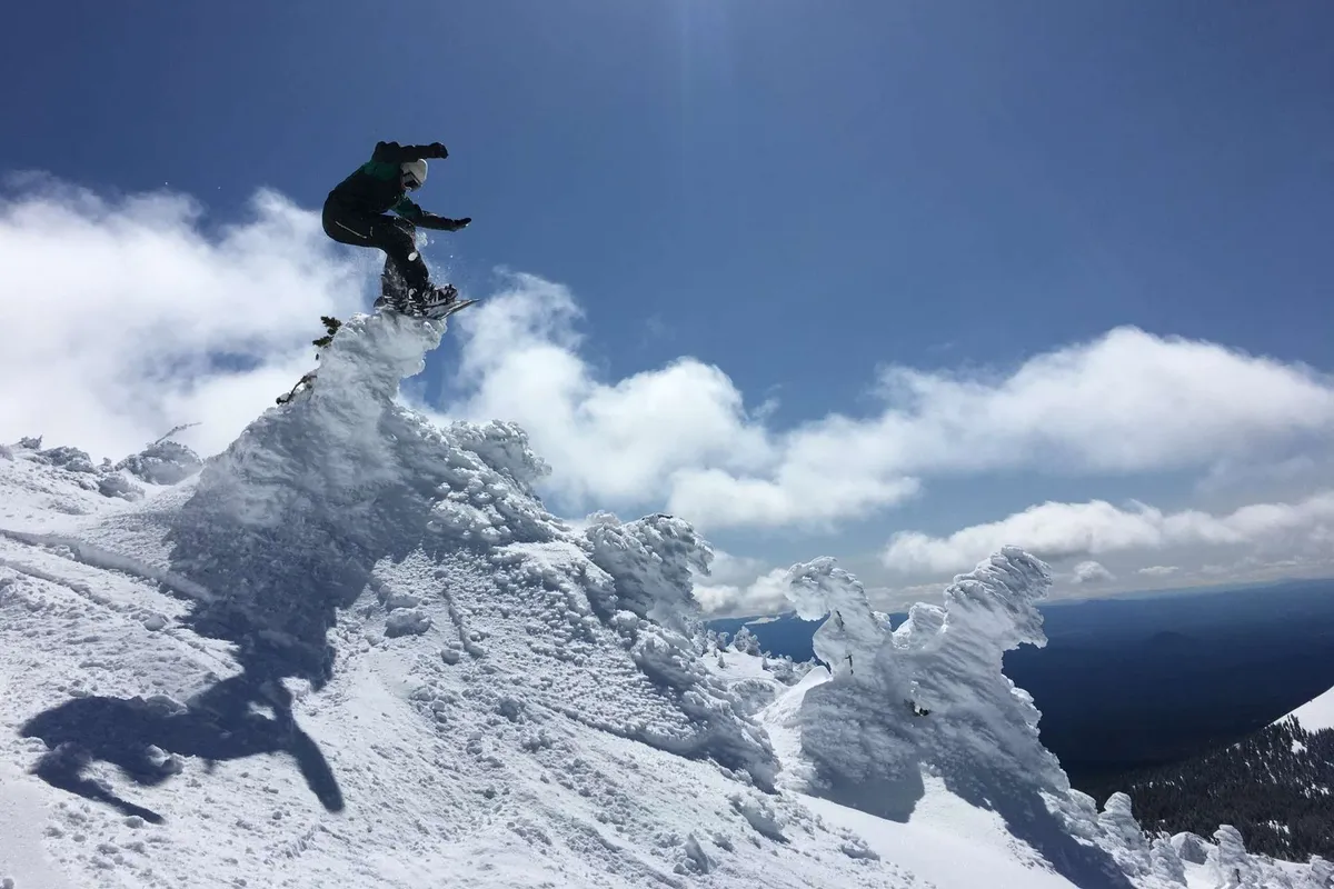 A snowboarder launches into the air against a dramatic backdrop of snow-covered mountain peaks and clouds. The image exudes excitement and captures the winter sports possibilities described in the section.